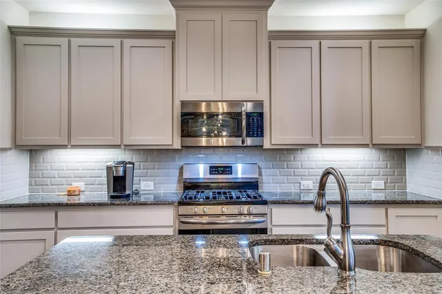 a kitchen with stainless steel appliances granite countertop a sink a stove and a white cabinets
