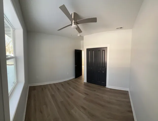 an empty room with wooden floor ceiling fan and windows