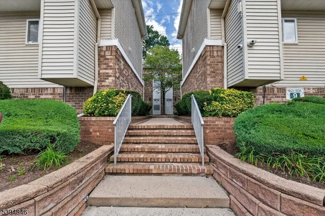 a view of a white house with a small yard plants and a large tree