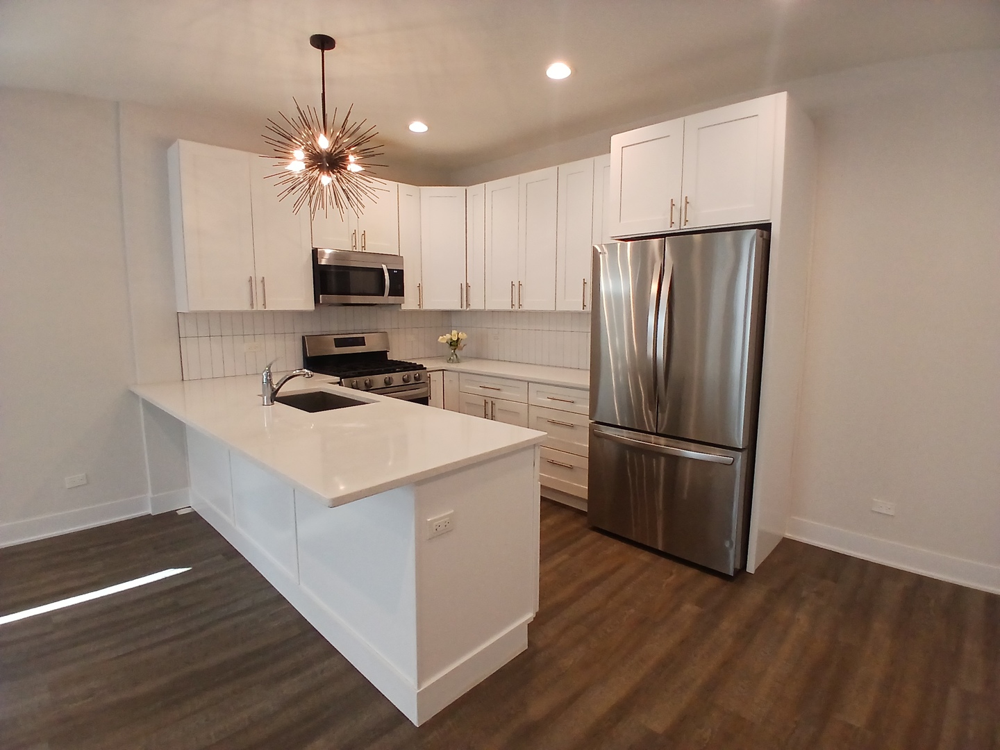 4608 South Indiana Avenue, Unit 1 Chicago, IL 60653 - Photo 7 of 24 a kitchen that has a microwave a stove a refrigerator a sink and white cabinets with wooden floor