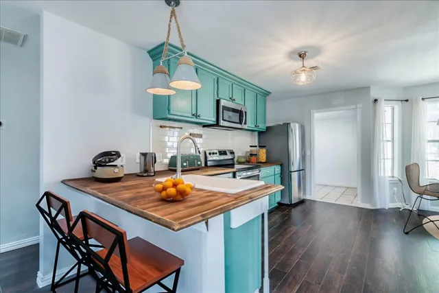 a kitchen with stainless steel appliances granite countertop a sink a stove a refrigerator a dining table and chairs with wooden floor