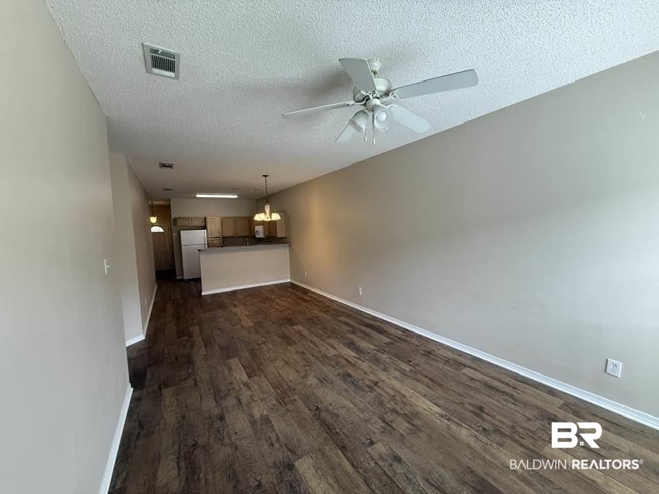 2651 South Juniper Street, Unit 401 Foley, AL 36535 - Photo 19 of 27 Unfurnished living room featuring dark wood-style floors, visible vents, baseboards, a textured ceiling, and ceiling fan with notable chandelier
