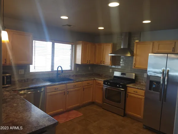 a kitchen with stainless steel appliances granite countertop a sink a stove a refrigerator cabinets and a window