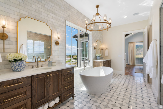 115 East Hidden Ridge Lane, Unit 42 Mapleton, UT 84664 - Photo 24 of 103 Freestanding soaking tub with large windows, patterned floor tiling, marble-topped dual vanity, and a brass chandelier