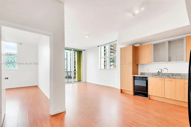 an empty room with wooden floor and a kitchen