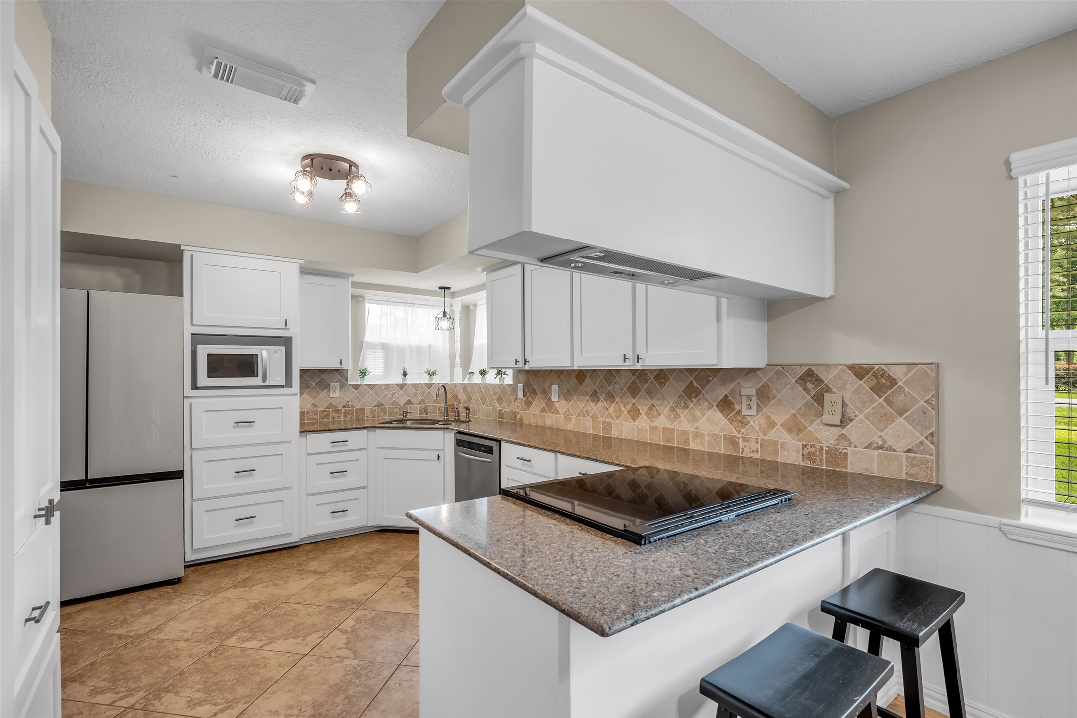 22502 Fields Lane Spring, TX 77389 - Photo 12 of 39 This kitchen features modern stainless steel appliances, white cabinetry, and a stylish tile backsplash. It has a cozy breakfast bar with seating and ample natural light from a large window. The layout is functional and welcoming.