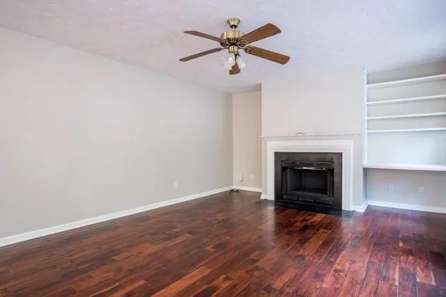 a view of an empty room with wooden floor fireplace and a window