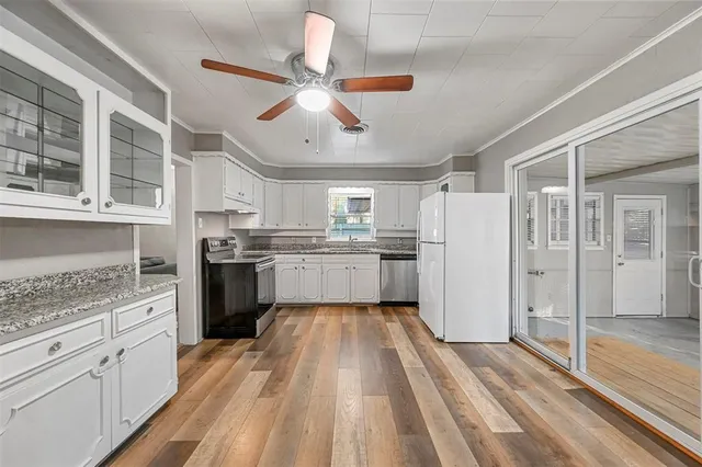 a kitchen with stainless steel appliances granite countertop a refrigerator a sink dishwasher a stove and white countertops with wooden floor