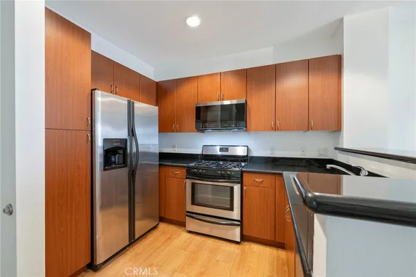 a kitchen with stainless steel appliances granite countertop a refrigerator a stove and a sink with wooden cabinets