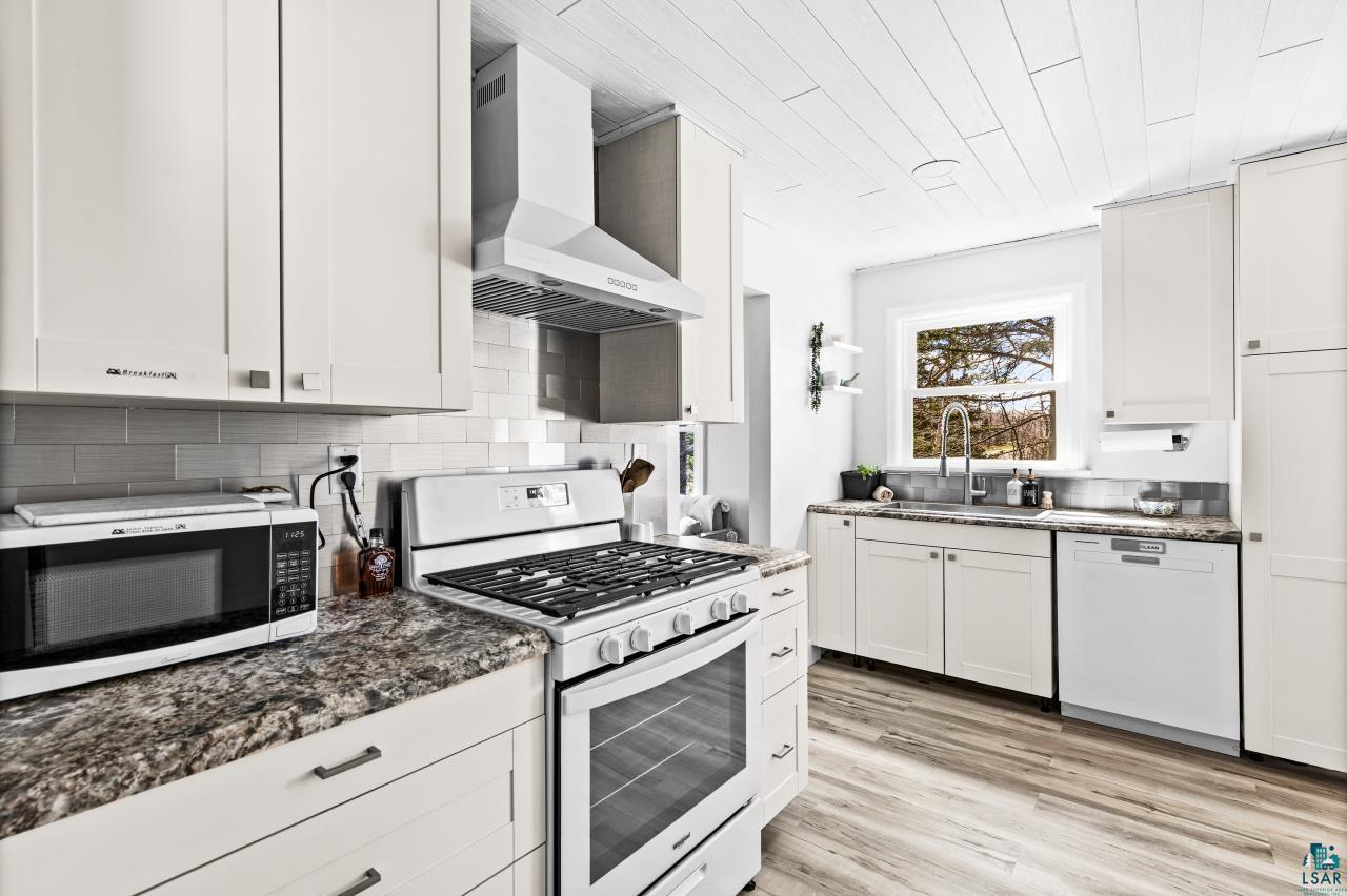 3645 Haines Road Hermantown, MN 55811 - Photo 27 of 35 Contemporary kitchen featuring white cabinetry, stone-finish countertops, stainless steel appliances, a tile backsplash, and wood-finish flooring