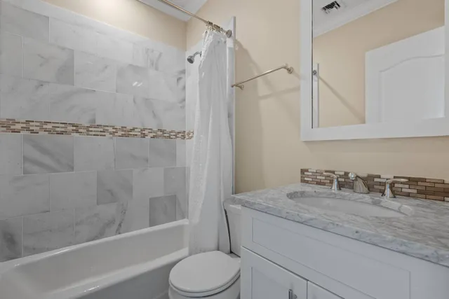 a bathroom with a granite countertop bathtub shower sink vanity and toilet