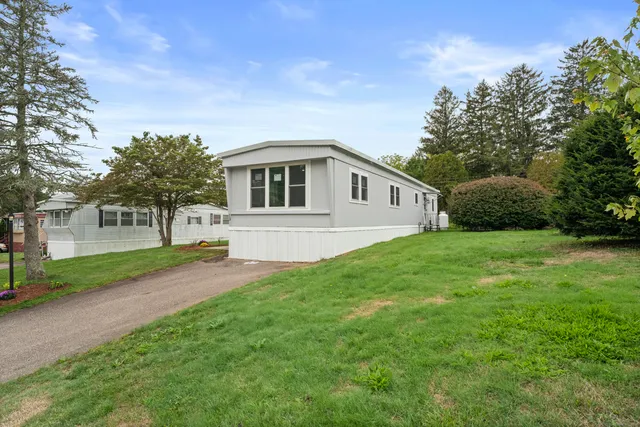 a house that is sitting in the grass with large trees and plants