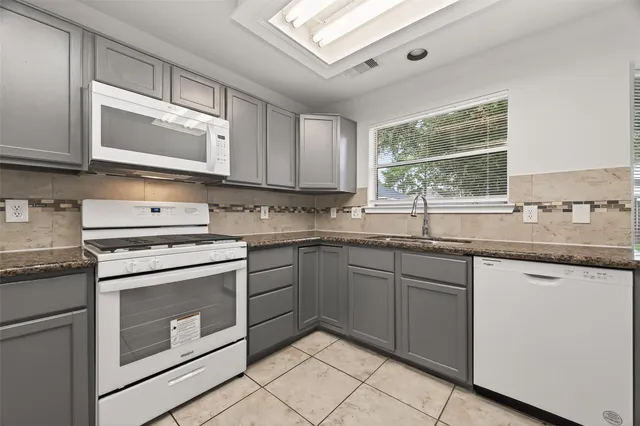 a kitchen with granite countertop white cabinets white stainless steel appliances a sink and a window