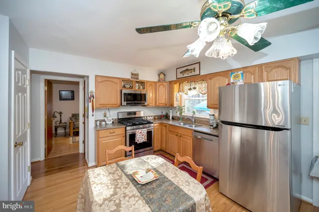 a kitchen with stainless steel appliances granite countertop a refrigerator a stove a sink dishwasher and a dining table with wooden floor