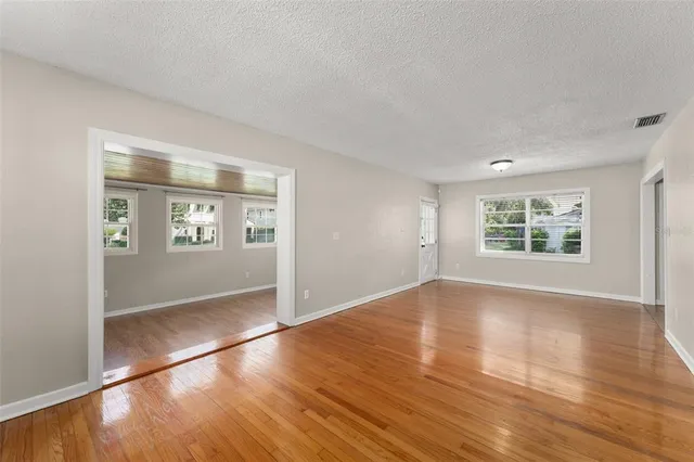 an empty room with wooden floor kitchen view and windows