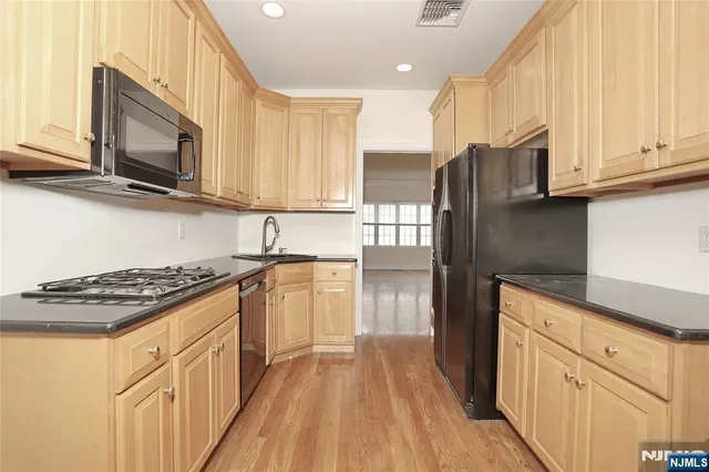 a kitchen with stainless steel appliances granite countertop a stove top oven a sink dishwasher and a refrigerator with wooden cabinets