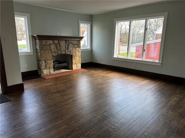 an empty room with wooden floor fireplace and windows