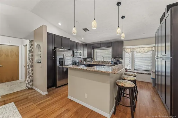 a kitchen with stainless steel appliances granite countertop a refrigerator a sink dishwasher a stove and white cabinets with wooden floor