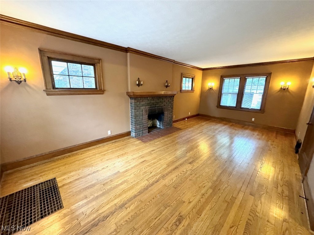 1011 Rushleigh Road Cleveland, OH 44121 - Photo 4 of 27 Unfurnished living room featuring light hardwood flooring, plenty of natural light, ornamental molding, and a fireplace