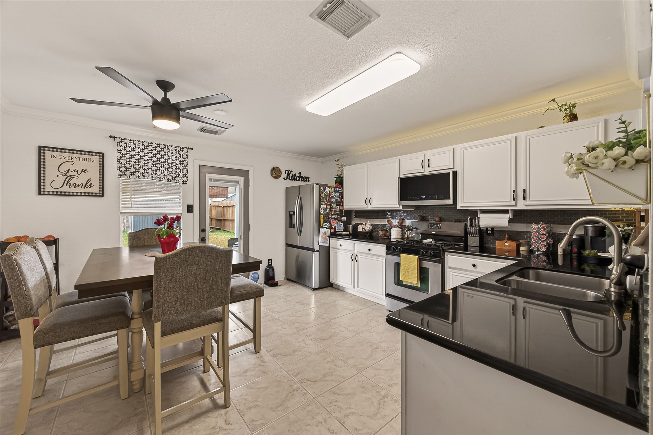 9902 Victoria Point Lane Houston, TX 77075 - Photo 10 of 35 This kitchen features modern appliances, white cabinetry, and sleek black countertops. A dining area with a ceiling fan is adjacent, and there's access to a backyard through a glass door, creating a bright and functional space.