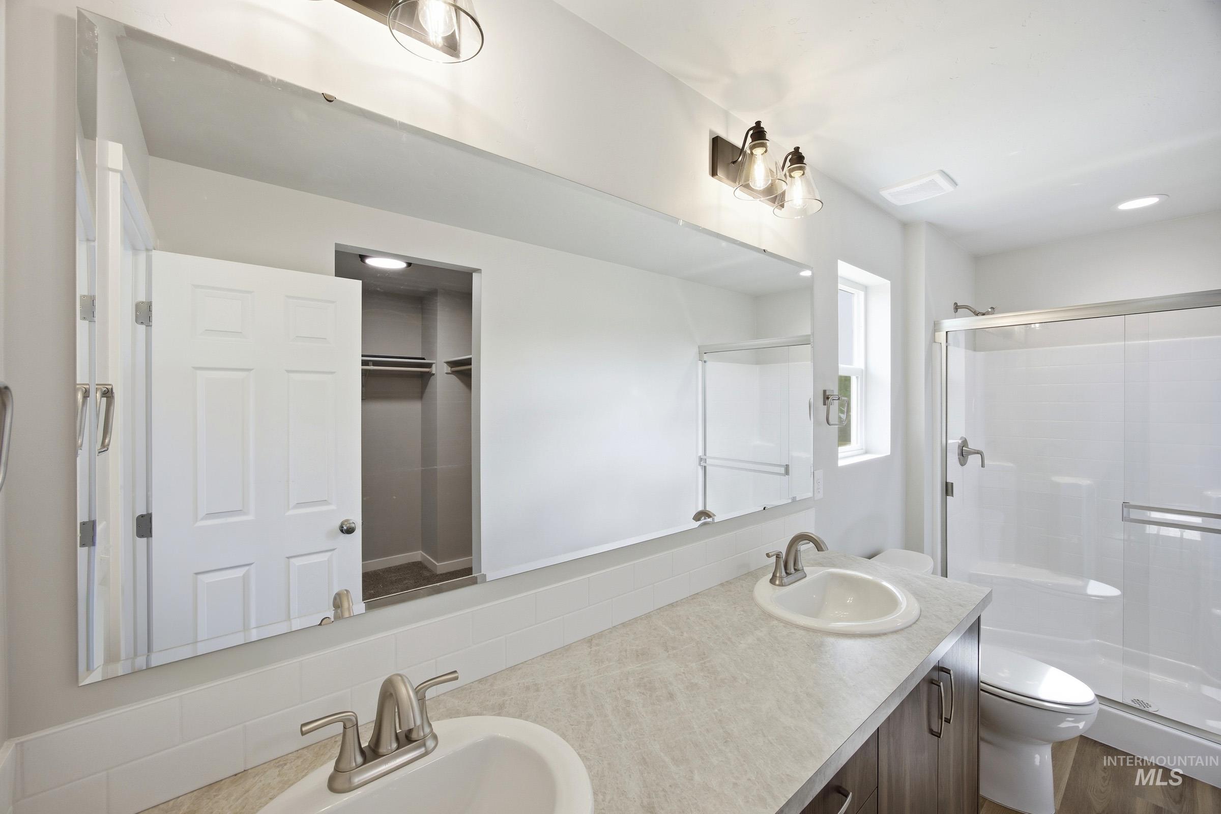 14044 Shiny Spruce Street Caldwell, ID 83607 - Photo 17 of 24 Bathroom featuring a double vanity with undermount sinks, a large wall-mounted mirror, a shower with a sliding glass door, and a toilet