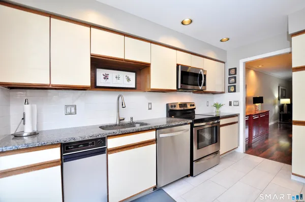 a kitchen with stainless steel appliances granite countertop a stove top oven a sink dishwasher and white cabinets with wooden floor