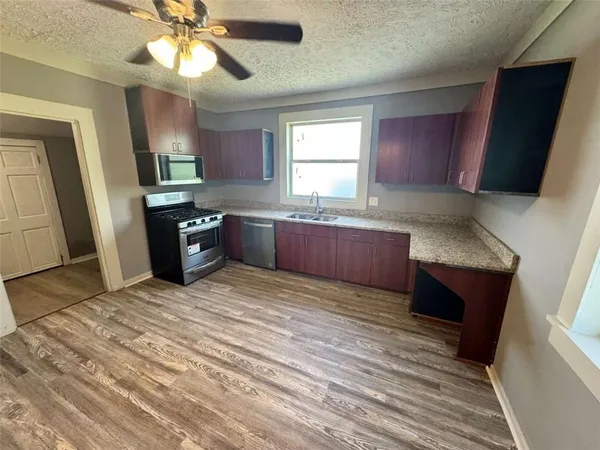 a kitchen with stainless steel appliances granite countertop a refrigerator a sink dishwasher a stove and white countertops with wooden floor