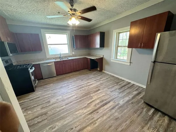 a kitchen with stainless steel appliances granite countertop a refrigerator a sink dishwasher a stove and white countertops with wooden floor