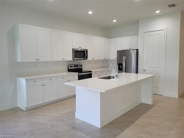 a kitchen with kitchen island a white counter top space stainless steel appliances and cabinets