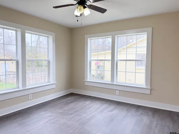 an empty room with chandelier fan and windows