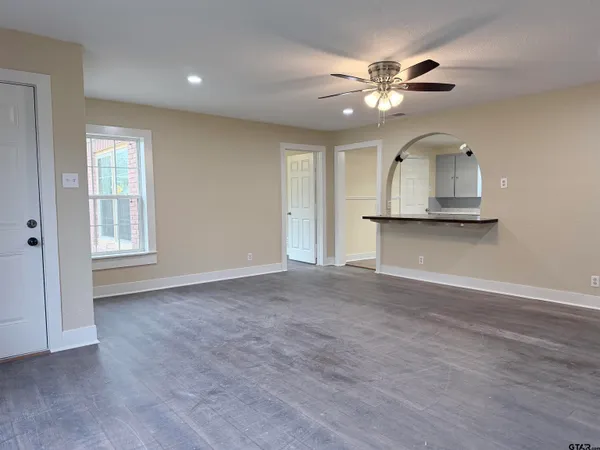 an empty room with wooden floor ceiling fan and windows