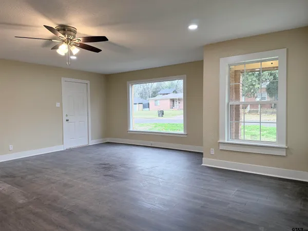 an empty room with wooden floor chandelier fan and windows