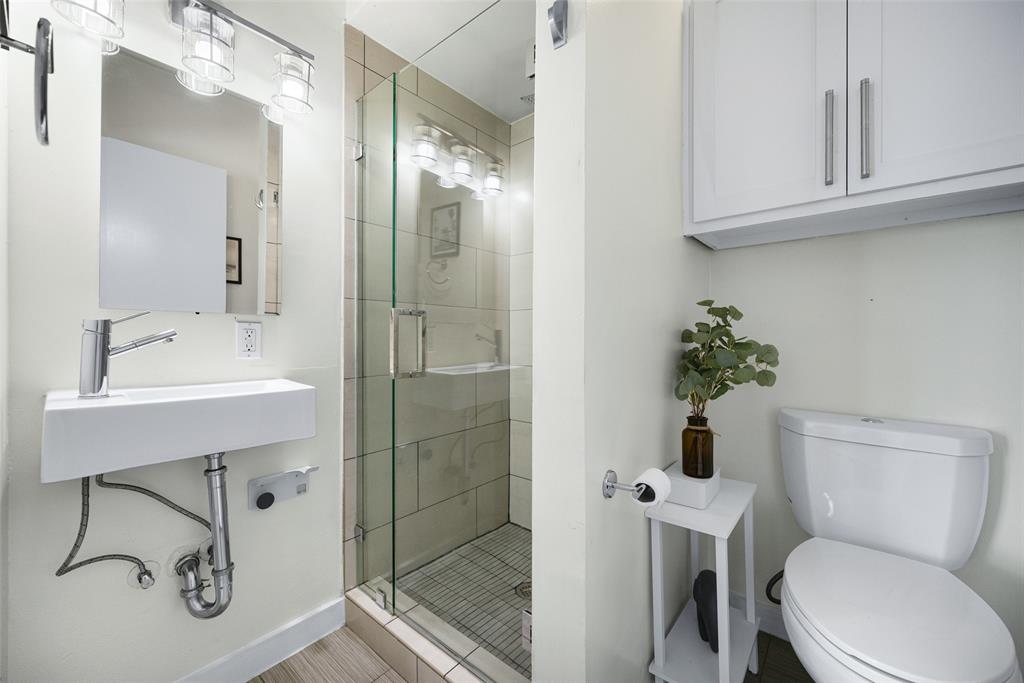 3922 Gilbert Avenue, Unit 214 Dallas, TX 75219 - Photo 17 of 27 White floating vanity with a chrome faucet, illuminated mirror, and glass-enclosed shower with tiled walls