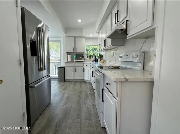 a kitchen with stainless steel appliances granite countertop a refrigerator a sink dishwasher a stove and white countertops with wooden floor