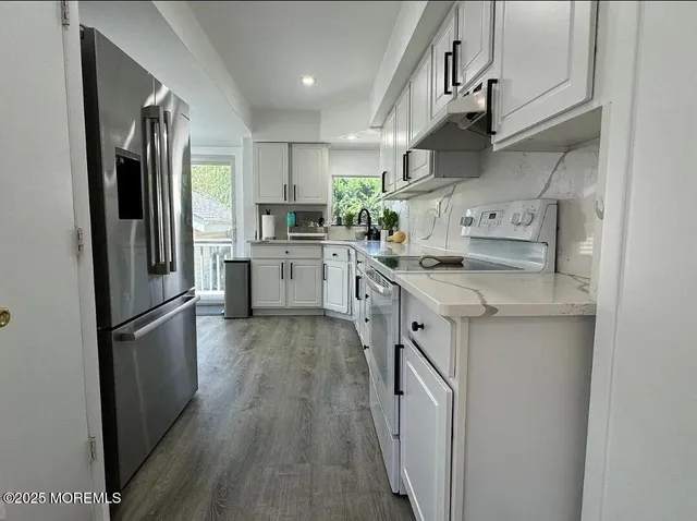 a kitchen with stainless steel appliances granite countertop a refrigerator a sink dishwasher a stove and white countertops with wooden floor