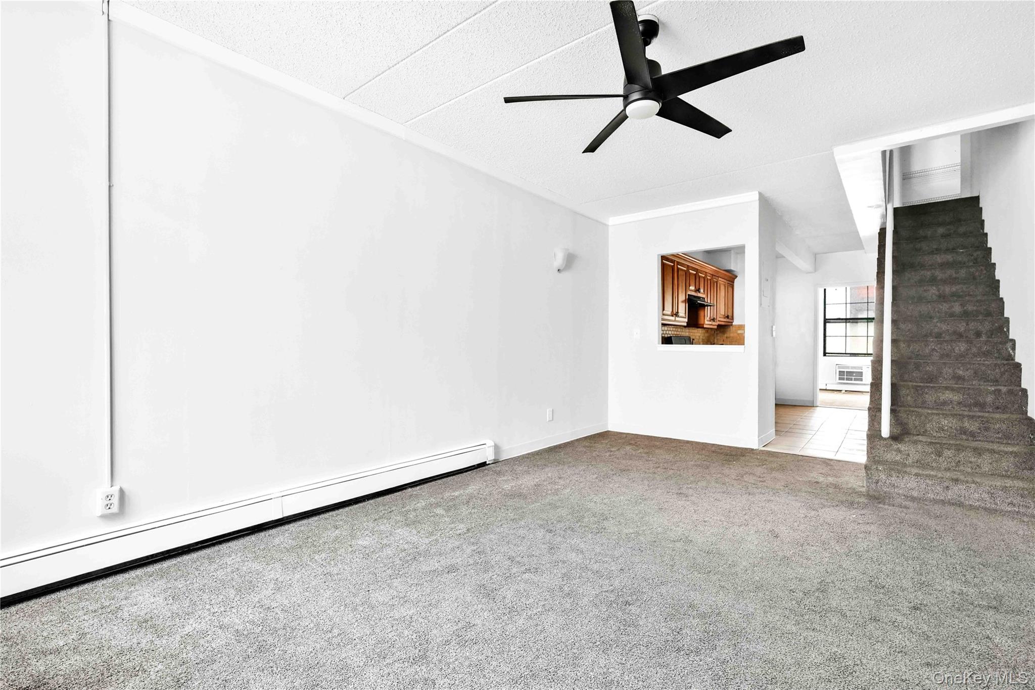 758 Brook Avenue, Unit 56C Bronx, NY 10455 - Photo 5 of 16 Unfurnished living room featuring a baseboard radiator, light colored carpet, a ceiling fan, and stairway