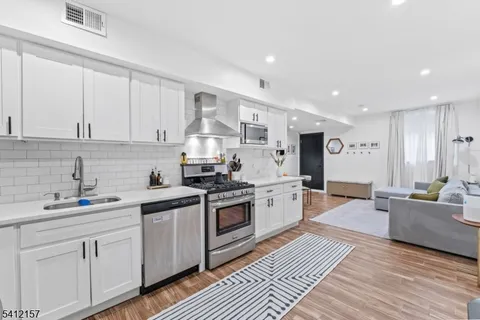 a kitchen with stainless steel appliances granite countertop a sink dishwasher stove and white cabinets with wooden floor