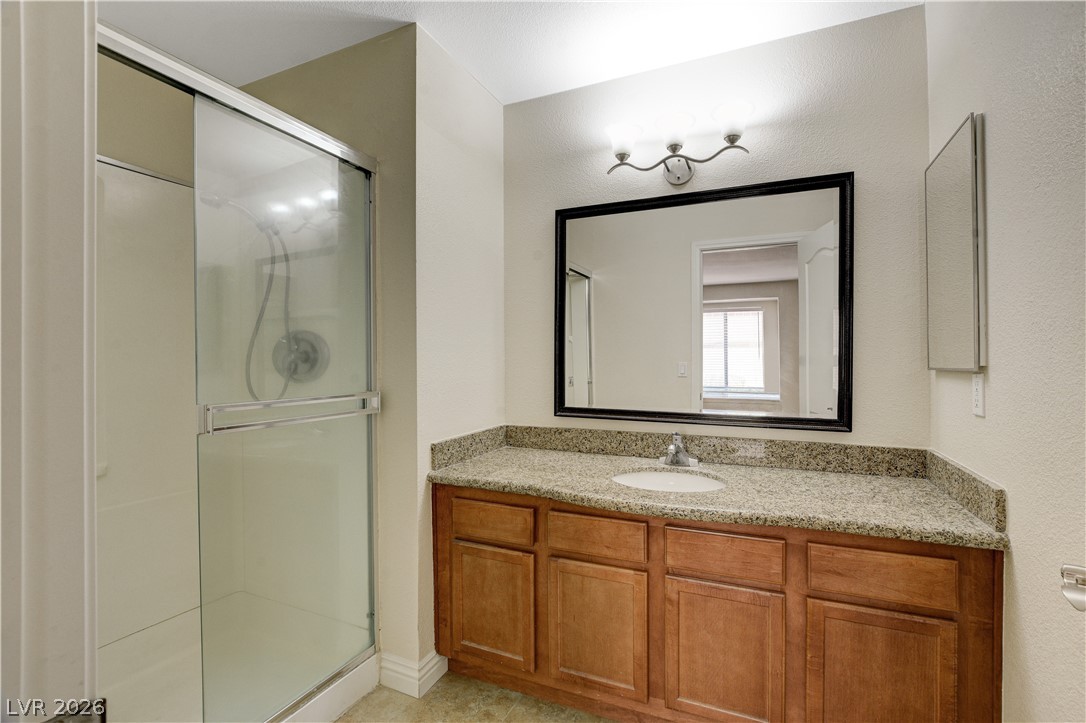 7200 West Pirates Cove Road, Unit 1026 Las Vegas, NV 89145 - Photo 26 of 35 This bathroom features a sleek glass-enclosed shower and a vanity with a granite countertop.