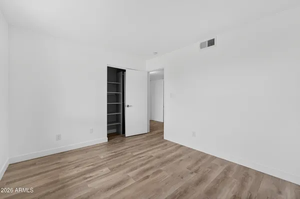a view of an empty room with wooden floor & closet