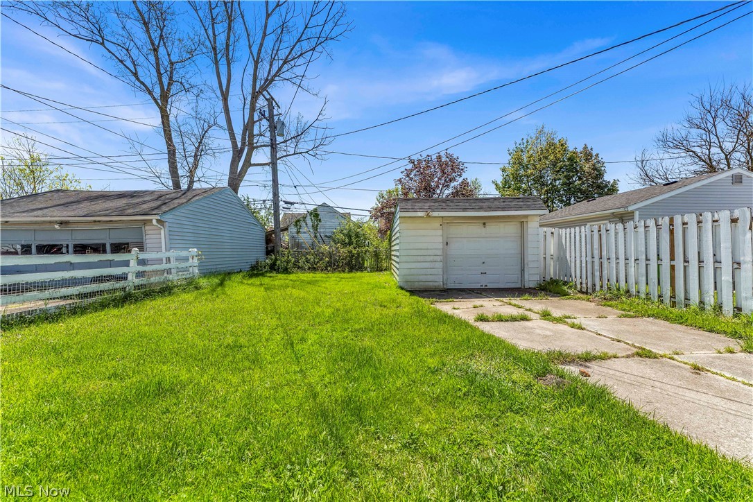 12808 Havana Road Cleveland, OH 44125 - Photo 19 of 19 Expansive grassy yard area featuring a detached shed with a garage door, a concrete driveway, and a white picket fence