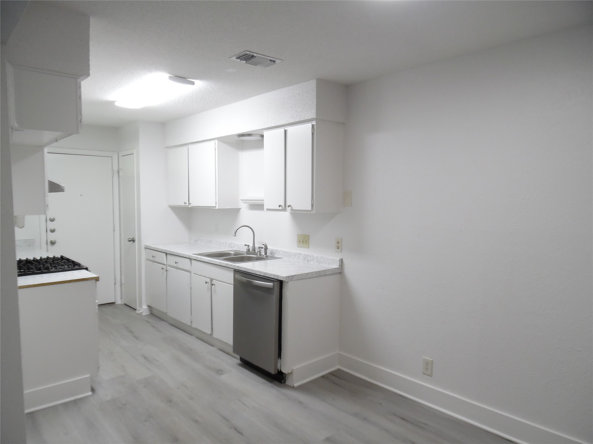 7400 Dixie Drive, Unit B Austin, TX 78744 - Photo 8 of 15 Kitchen featuring wood-finish flooring, white cabinetry, a stainless steel dishwasher, and a gas range