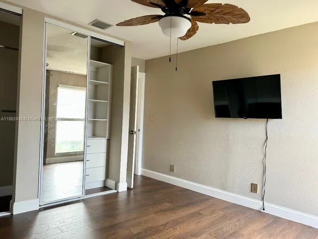 a view of an empty room with wooden floor and a ceiling fan