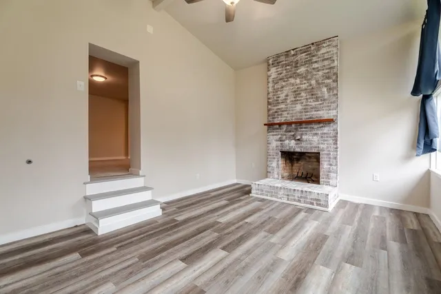a view of an empty room with wooden floor fireplace and a window
