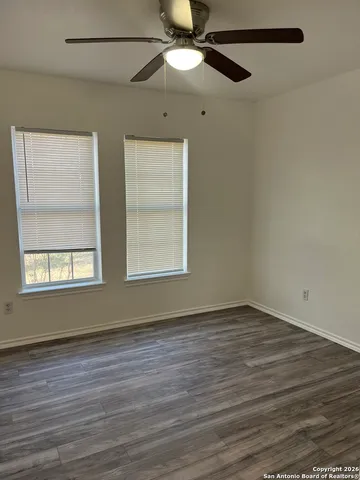 an empty room with wooden floor fan and windows