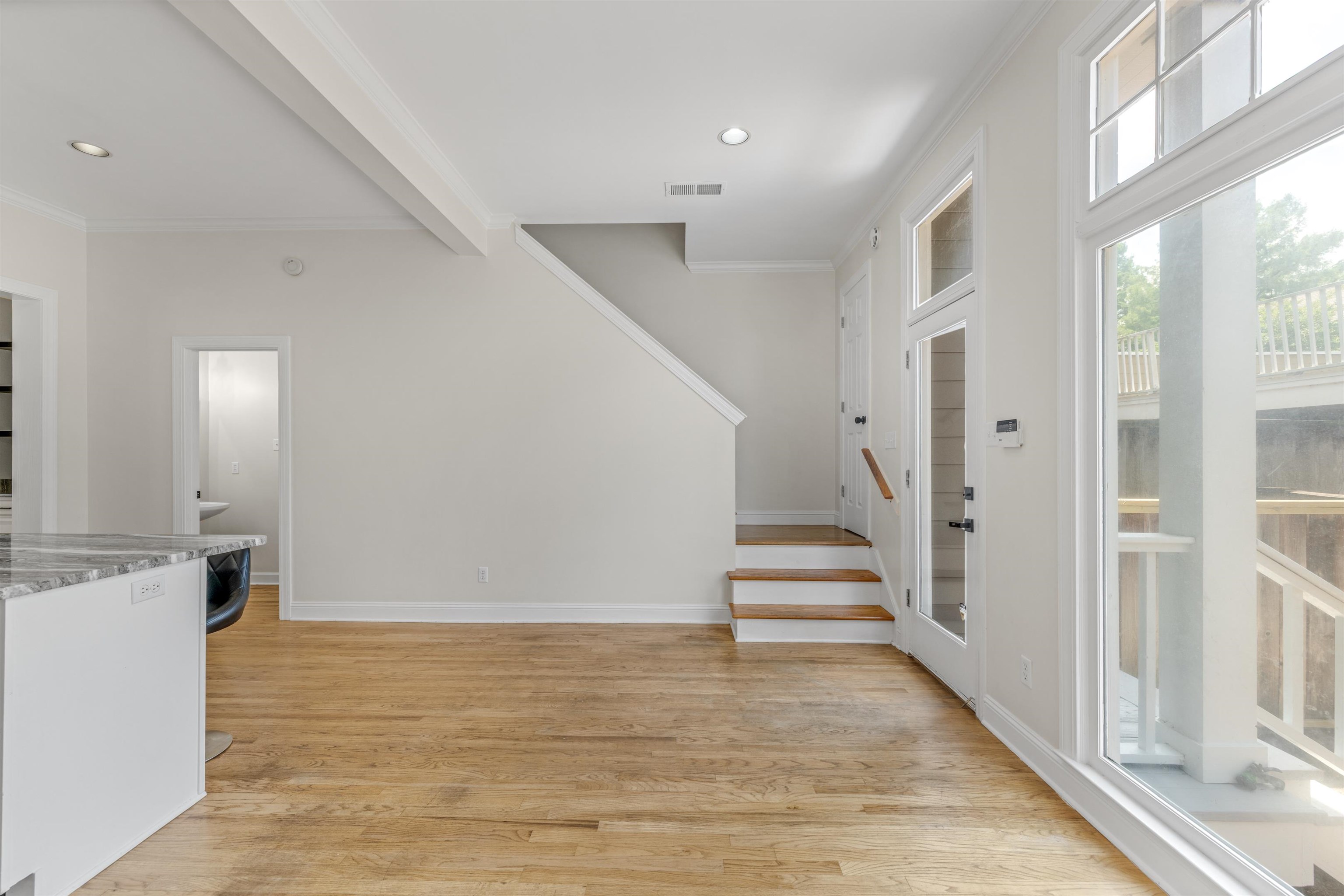 921 Harbor View Drive Memphis, TN 38103 - Photo 14 of 33 Open-concept living space featuring hardwood flooring, a white kitchen island with a stone countertop, an illuminated stairwell with wood steps and a handrail, and large windows with transom panels