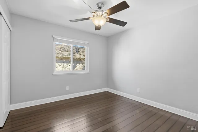 an empty room with wooden floor chandelier fan and windows