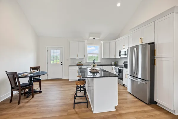 a kitchen with stainless steel appliances granite countertop a refrigerator a stove a sink a dining table and chairs with wooden floor