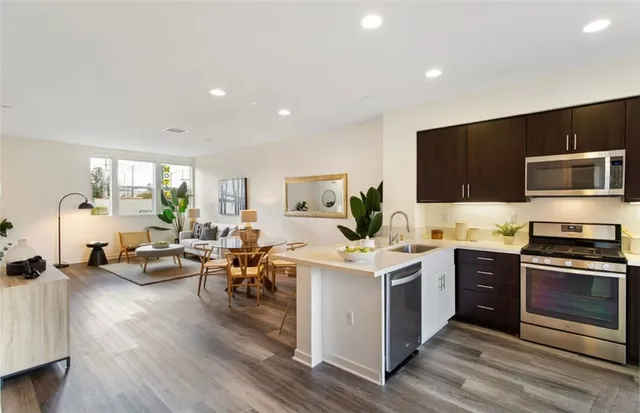 a open kitchen with stainless steel appliances a stove top oven a sink dishwasher and a refrigerator with wooden floor