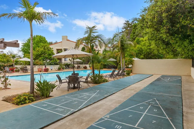 a view of a patio with couches and table and chairs under an umbrella with palm trees