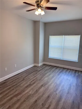 an empty room with wooden floor chandelier fan and windows